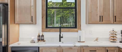 A kitchen with wooden cabinets, a black faucet, a window with blinds, and a white countertop.