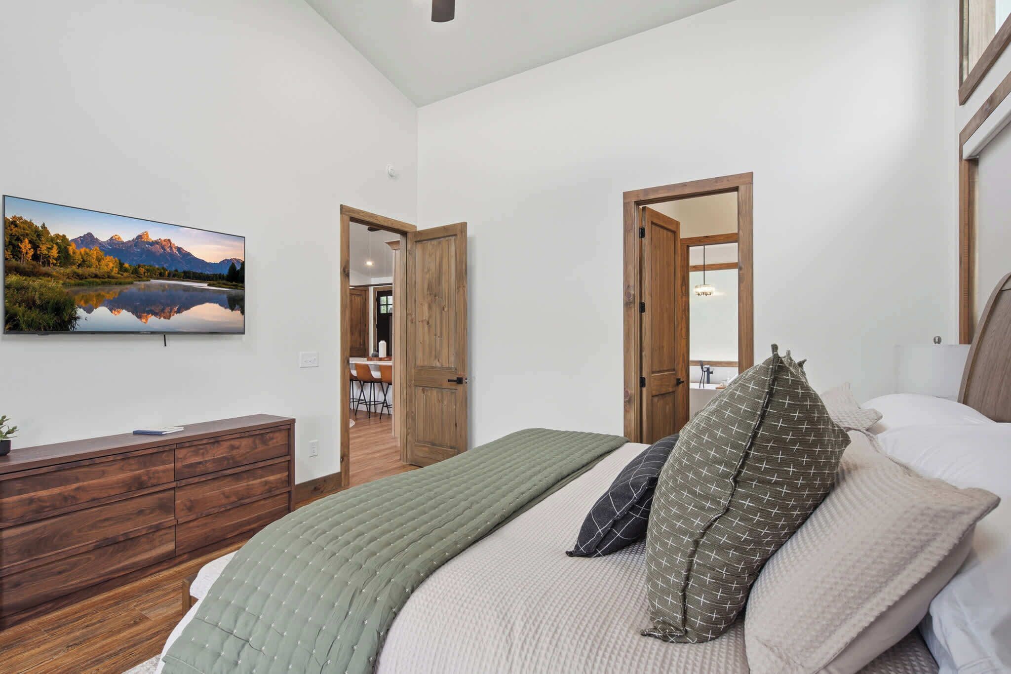 A bedroom with a bed, a dresser, a painting, and two doors leading to other rooms.
