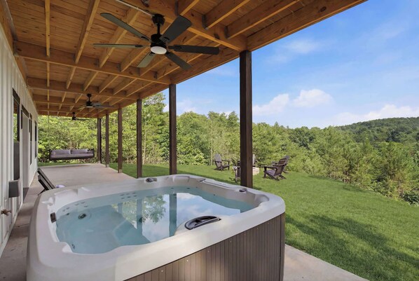 A hot tub under a wooden deck with a view of a grassy landscape. - The Lodge at Walnut Peak (Mineral Bluff)