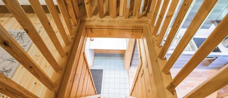 A wooden staircase leading to an upper floor with a view of a tiled floor and a window.