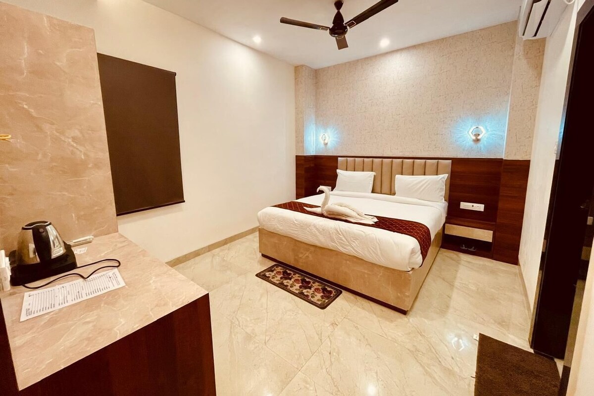 A hotel room with a bed, bedside tables, a desk with a kettle, and a ceiling fan.