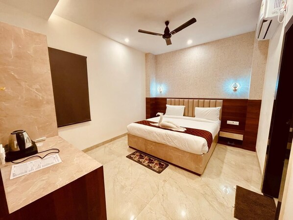 A hotel room with a bed, bedside tables, a desk with a kettle, and a ceiling fan.
