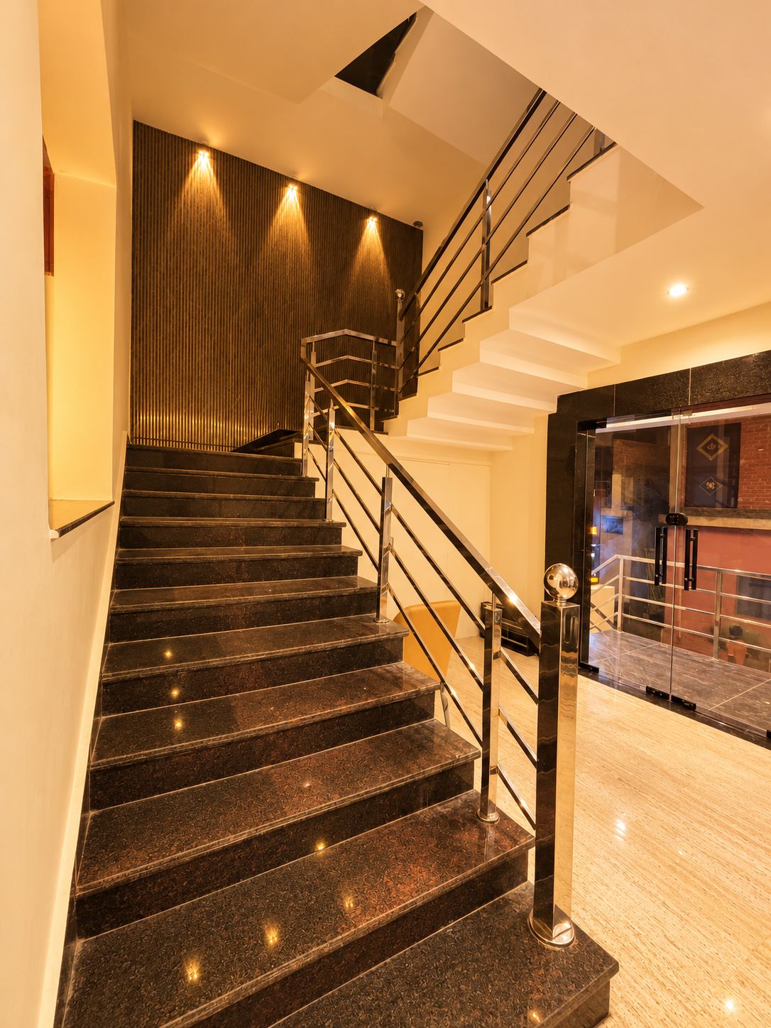 Una escalera moderna con barandilla de vidrio y suelo de piedra pulida.
