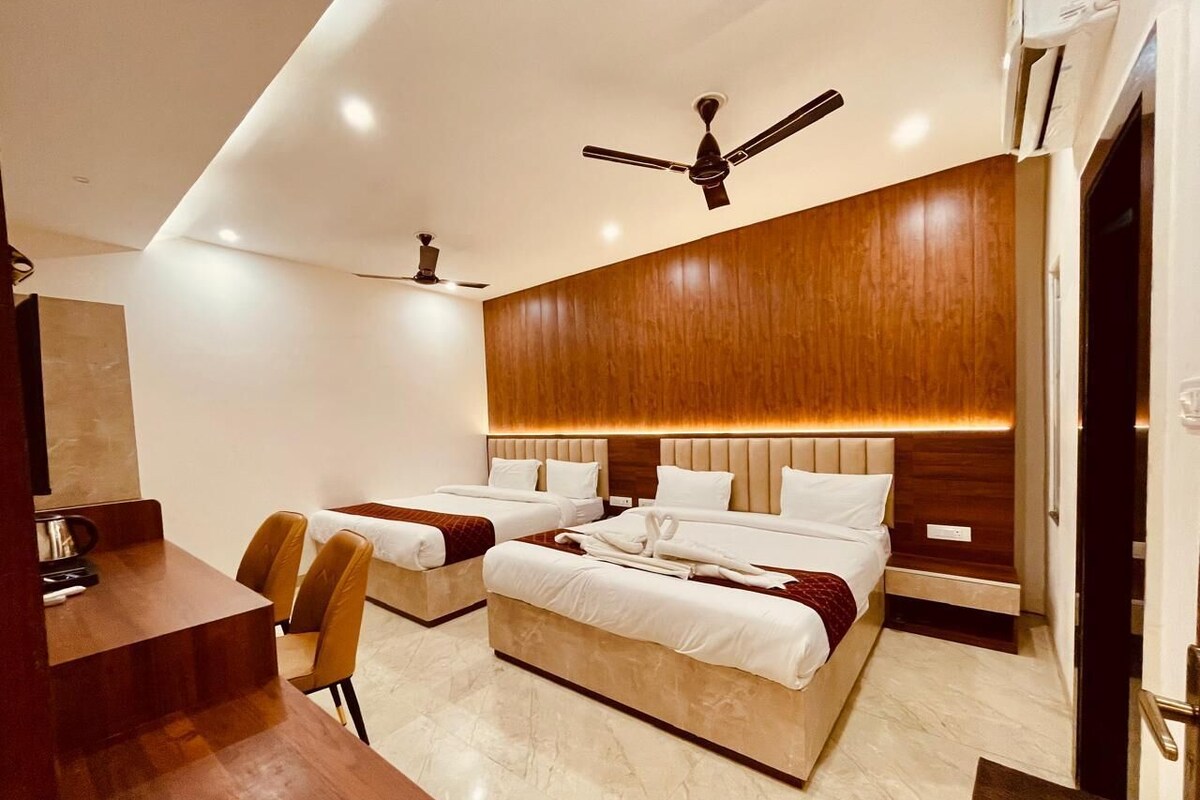 A hotel room with two beds, a desk, chairs, a ceiling fan, and a wooden accent wall.
