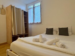 A bedroom with a bed, pillows, a wooden wardrobe, and a window with curtains. - Superbe appt 3 ch à 2 pas du circuit des 24H (Le Mans)