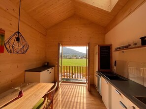 A wooden interior with a dining area, kitchen, and a balcony with a view of a green landscape and mountains. - "Holz und Himmel" Vacation Rental for 2 People with Open-Concept Living Room and Bedroom, 53 m² (Aschau im Chiemgau)