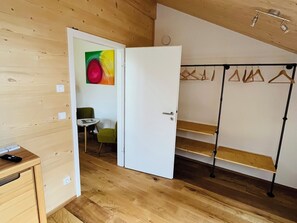 Ein Zimmer mit Holzboden, einer weißen Tür, einem grünen Stuhl, einem kleinen Tisch und einem Kleiderständer mit Kleiderbügeln.