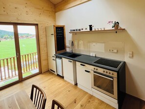 A kitchen with a black stove, white cabinets, a black sink, and a wooden floor. - "Holz und Himmel" Vacation Rental for 2 People with Open-Concept Living Room and Bedroom, 53 m² (Aschau im Chiemgau)