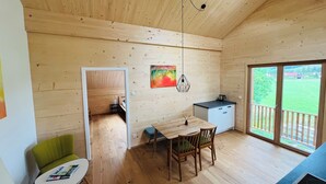 Interior em madeira com mesa de jantar, cadeiras, uma pequena cozinha e vista através de uma porta de vidro.