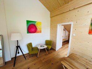 A room with wooden flooring, a green armchair, a small white table, a lamp, and a colorful abstract painting on the wall. - "Holz und Himmel" Vacation Rental for 2 People with Open-Concept Living Room and Bedroom, 53 m² (Aschau im Chiemgau)