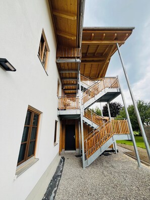 Un balcón de madera de varios niveles con una escalera de metal, una puerta y una ventana.