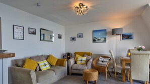 A living room with a sofa, armchairs, a coffee table, a dining table with chairs, a lamp, and framed pictures on the walls. - Sea Views Apartment in Ilfracombe (Ilfracombe)