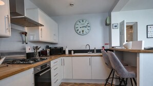 A modern kitchen with white cabinets, a wooden countertop, a gas stove, a microwave, and a clock on the wall. - Sea Views Apartment in Ilfracombe (Ilfracombe)