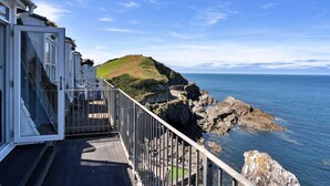 A coastal view with a rocky shoreline, a grassy hill, and a clear sky. - Sea Views Apartment in Ilfracombe (Ilfracombe)