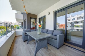 Ein Balkon mit einem Korbstuhl, einer grauen Couch, großen Fenstern und Blick auf andere Gebäude.