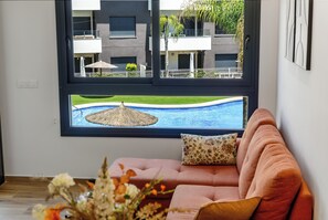 Ein modernes Wohnzimmer mit großem Fenster, einem rosafarbenen Sofa und Blick auf einen Swimmingpool und ein Gebäude.