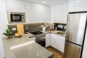 A modern kitchen with stainless steel appliances, white cabinetry, and a wooden bowl on the counter. - Charming 2-bedroom apartment with AC in tranquil Villamartín (Villamartín)