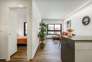 A modern apartment with a wooden floor, a bed with an orange bedspread, a dining area with a table and chairs, and a large window. - Charming 2-bedroom apartment with AC in tranquil Villamartín (Villamartín)