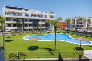 A hotel with a swimming pool surrounded by palm trees and umbrellas. - Charming 2-bedroom apartment with AC in tranquil Villamartín (Villamartín)