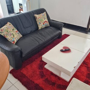 Ein schwarzes Ledersofa mit floralen Kissen, ein weißer Couchtisch mit Fernbedienung und ein roter Shaggy-Teppich in einem modernen Wohnzimmer.