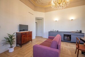 A living room with a sofa, a television on a cabinet, a potted plant, and a kitchen area with a stove and sink. - Luxury Boutique Apartment 2 in Palermo City Center with an Amazing View (Palermo)