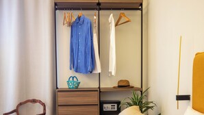 A hotel room with a bed, a wooden chair, a wardrobe with hanging clothes, a small table with a plant, and a bedside table with a lamp. - Luxury Boutique Apartment 2 in Palermo City Center with an Amazing View (Palermo)