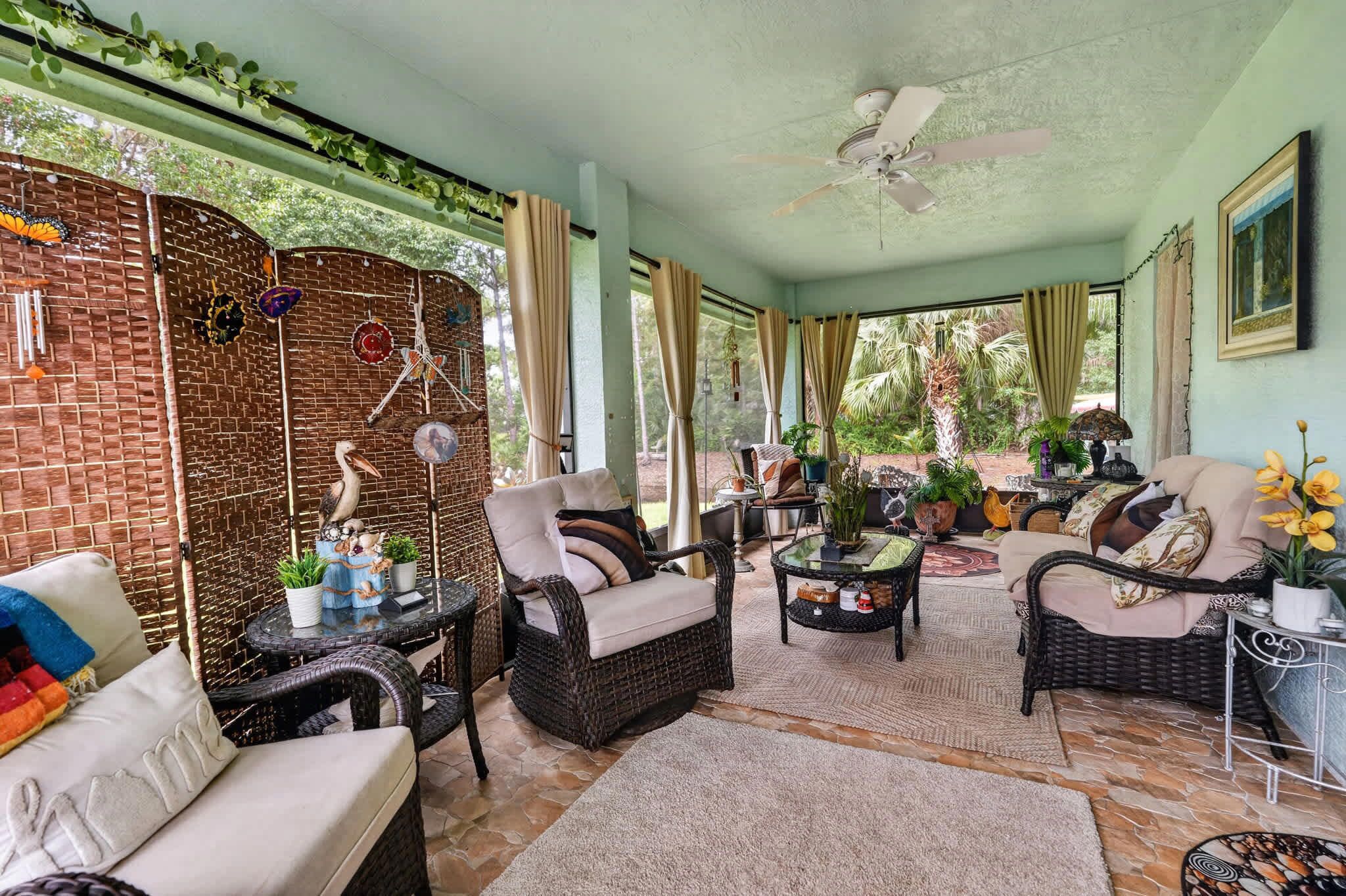 Un patio couvert aménagé avec des meubles en osier, un ventilateur de plafond et des plantes en pot.