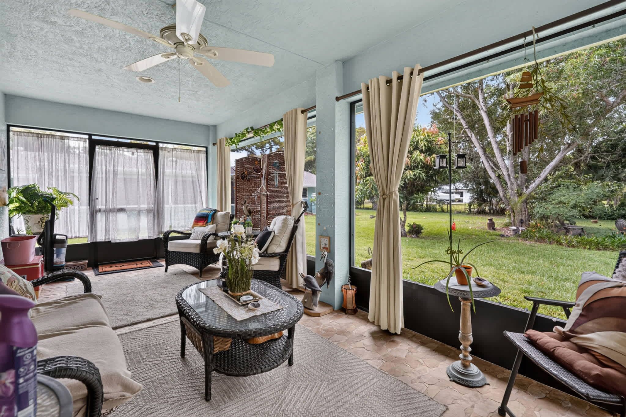 A covered patio with wicker furniture, a ceiling fan, and a view of a garden.