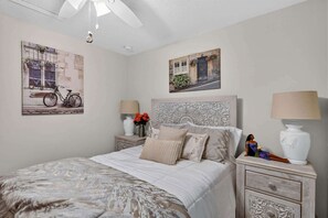 Une chambre à coucher comprenant un lit, deux tables de chevet, une commode, une lampe fixée au mur et deux œuvres d’art murales.