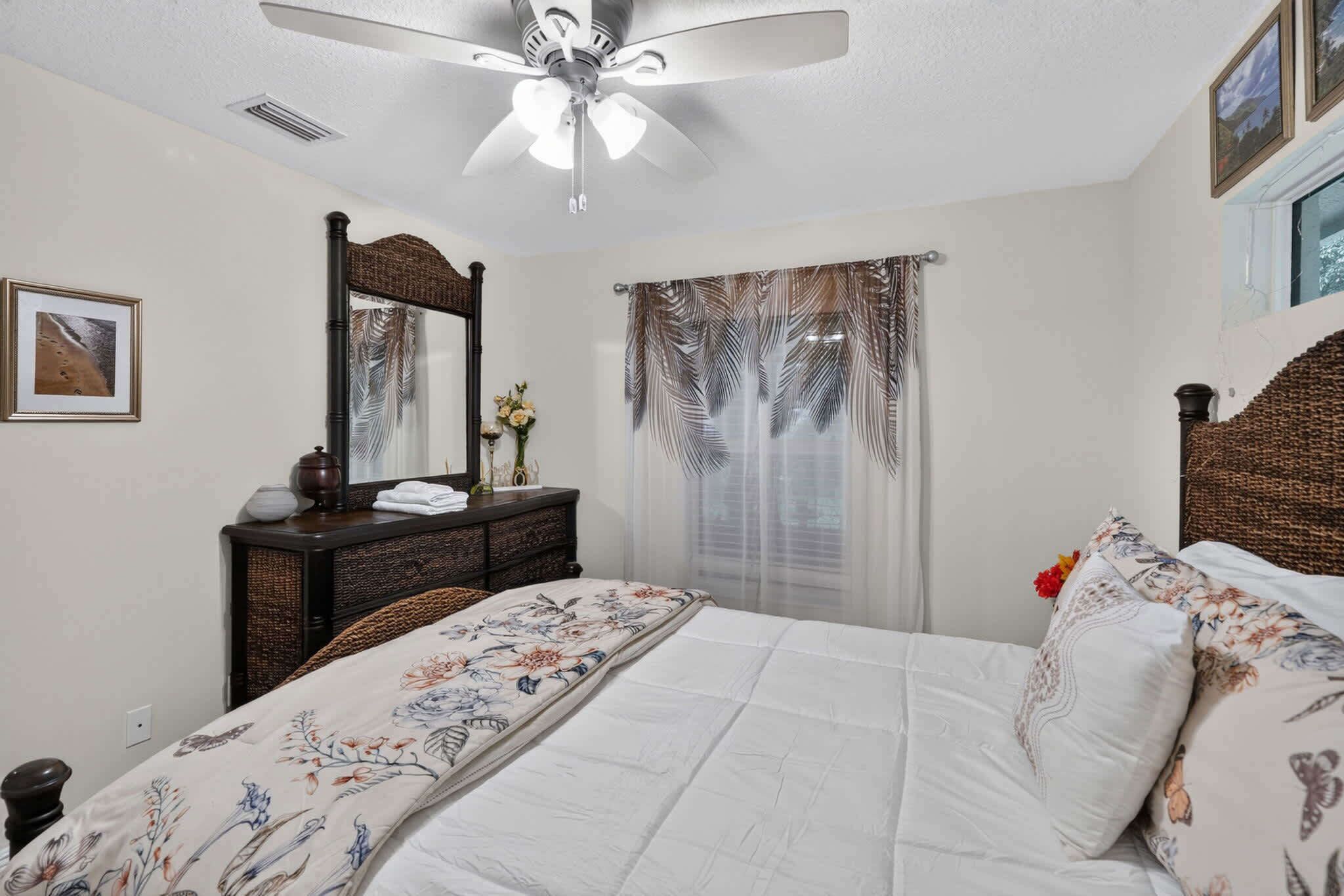 A bedroom with a bed, a ceiling fan, a dresser, a mirror, and a window with curtains.