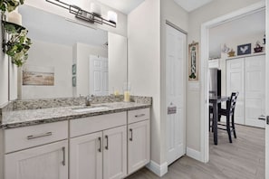 A modern bathroom with a large mirror, granite countertop, and white cabinetry.