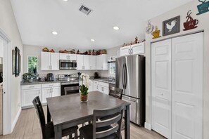 A modern kitchen with white cabinets, stainless steel appliances, and decorative items on the wall. - Abi's House - Private Jupiter Escape (Jupiter)