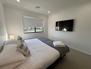 Un dormitorio con cama, ventana, televisor de pantalla plana y vista a un parque.