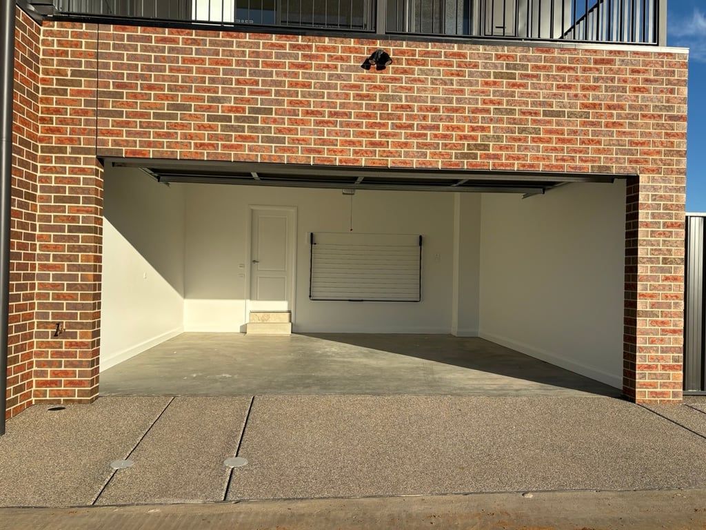 A garage with a closed roller door, a concrete floor, and a brick exterior.