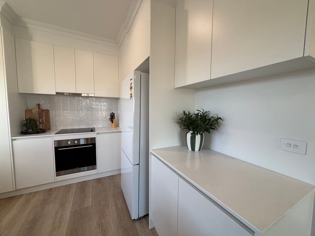 A modern kitchen with white cabinetry, a built-in oven, and a countertop with a potted plant.