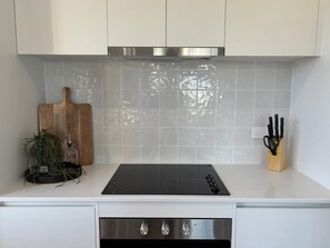 Una cocina con encimera blanca, placa de inducción negra, campana extractora de acero inoxidable y bloque de cuchillos.