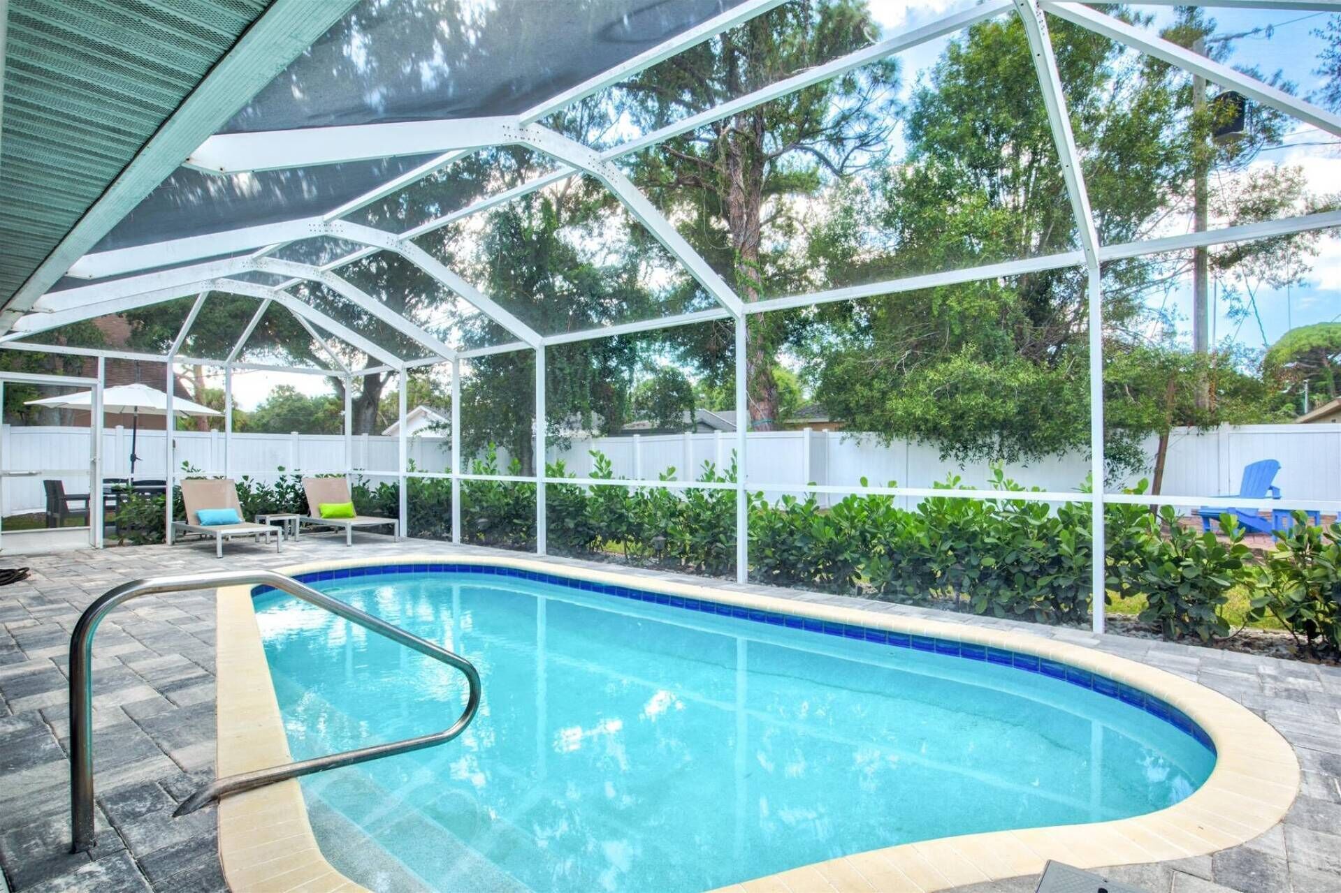 Ein Schwimmbecken mit weißer Liegefläche, umgeben von einer überdachten Terrasse mit Stühlen und Sonnenschirmen.
