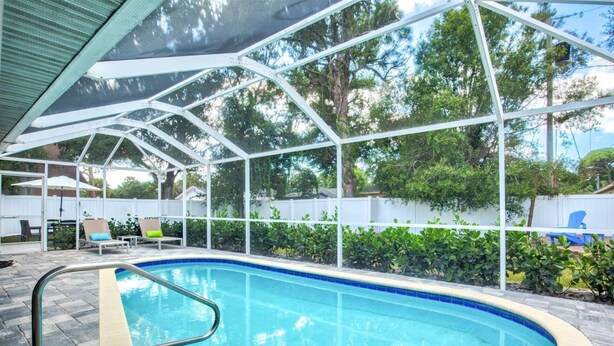 Piscina com deck branco, rodeada por um espaço coberto com espreguiçadeiras e guarda-sóis.