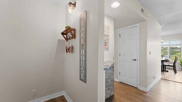 A hallway with a wooden coat rack, a wall-mounted sign reading 'LAKE HOUSE,' and a white door leading to a room with a view.