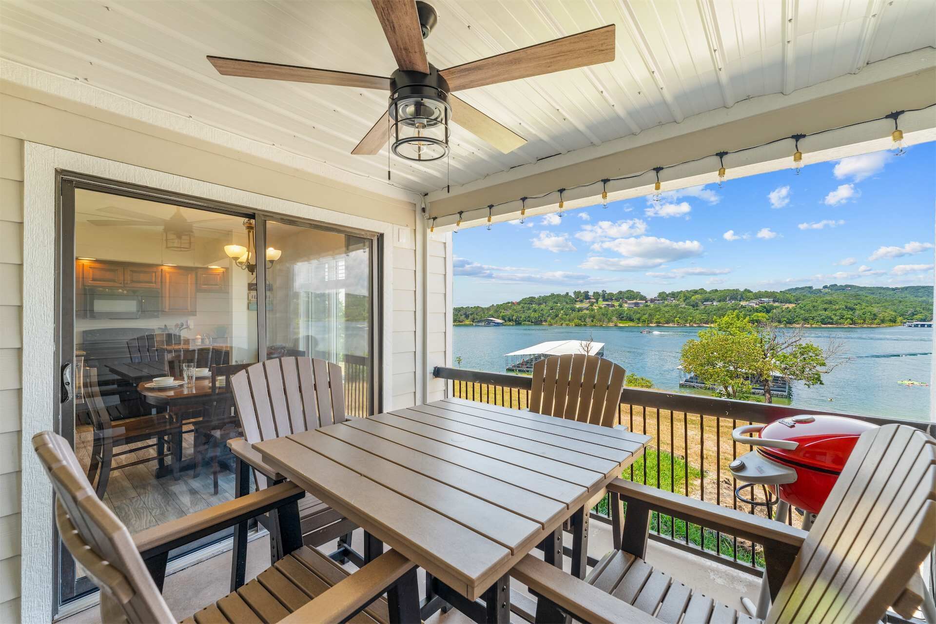 Un espace extérieur abrité, doté d’une table et de chaises, d’un ventilateur de plafond, et offrant une vue sur un lac et des collines.