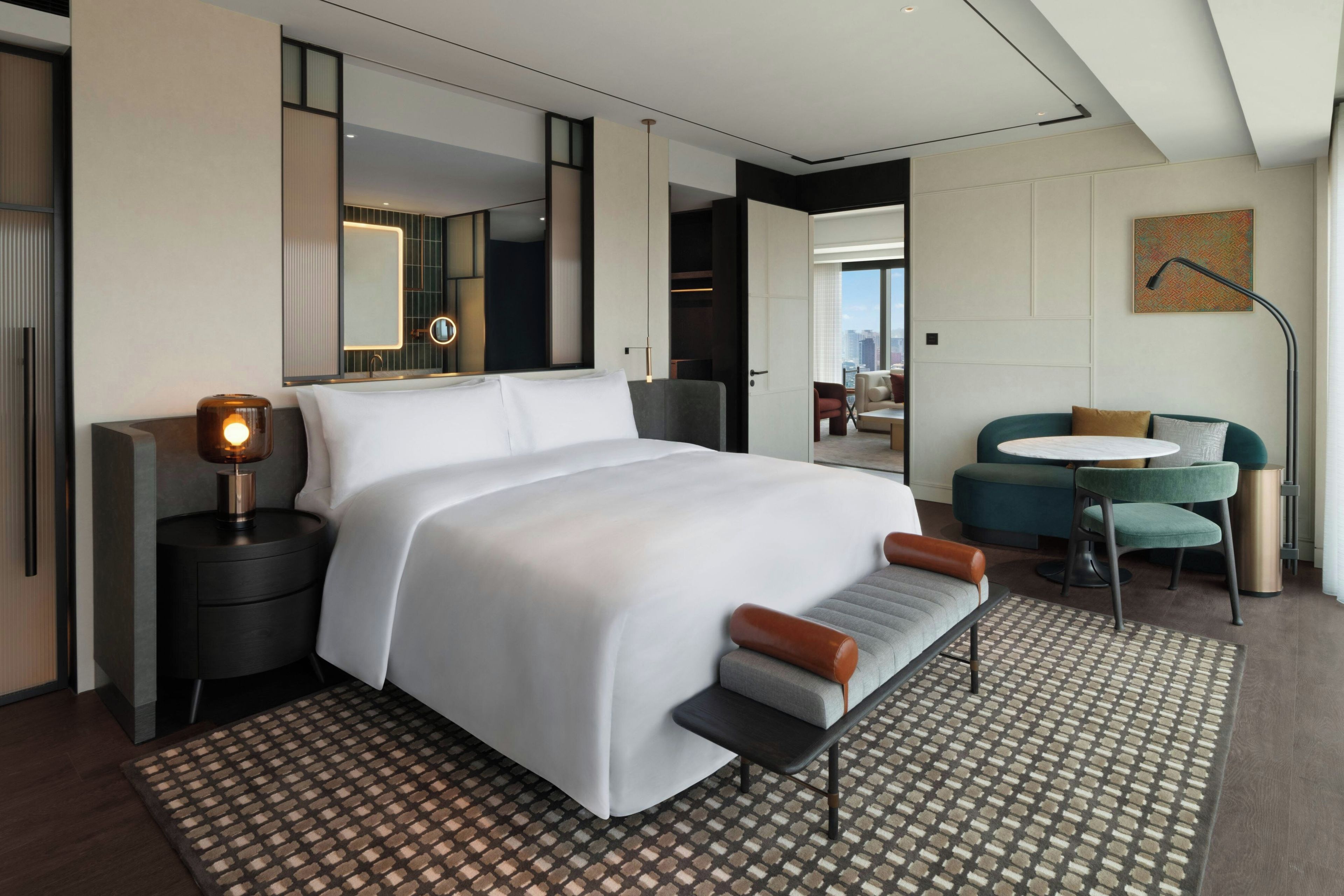 A modern hotel room with a large bed, bedside table, and a desk with a chair.