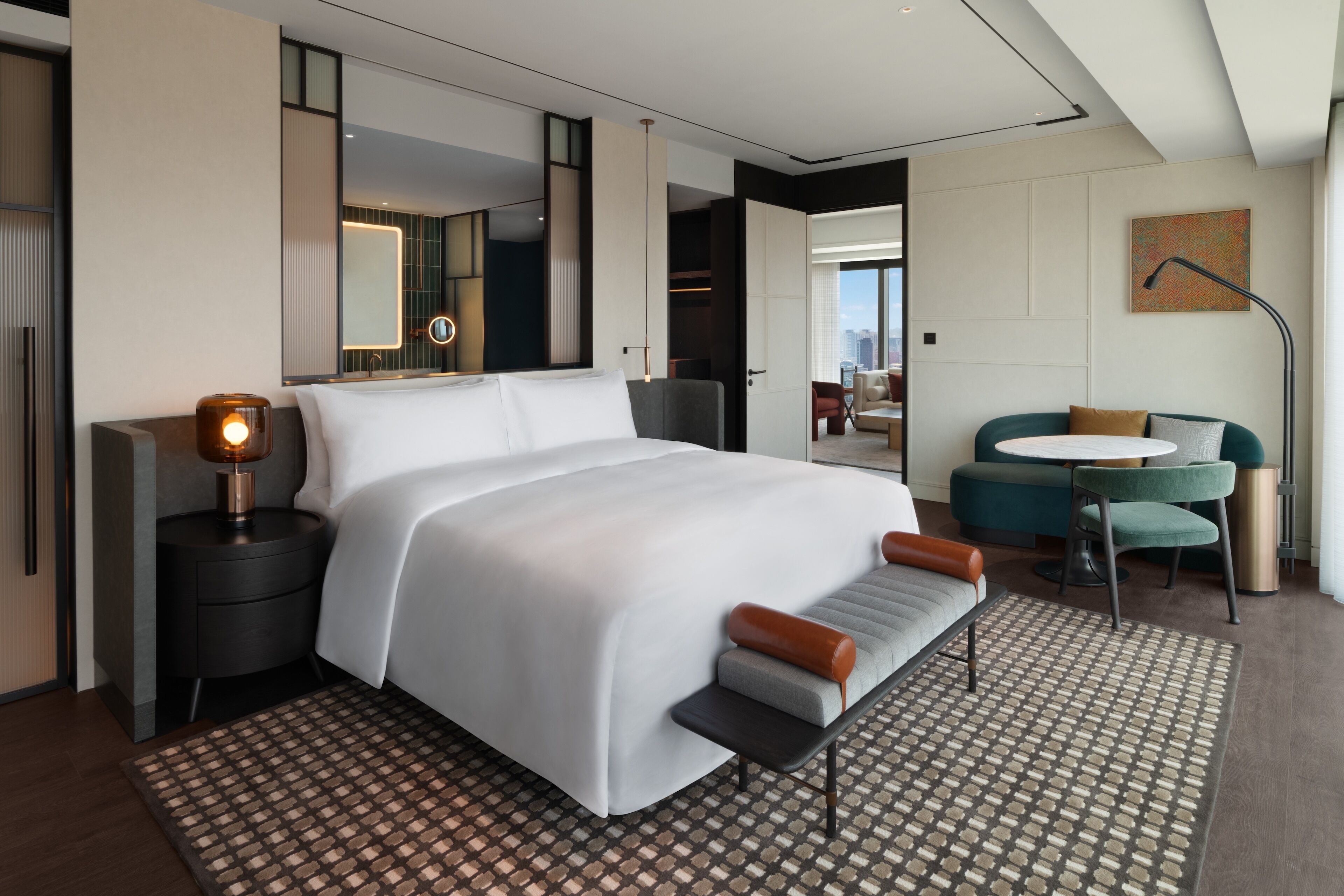A modern hotel room with a large bed, bedside tables, a desk, and a view of the city.