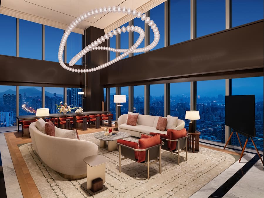 A modern living room with a city view, featuring a sofa, armchairs, a coffee table, and a TV.