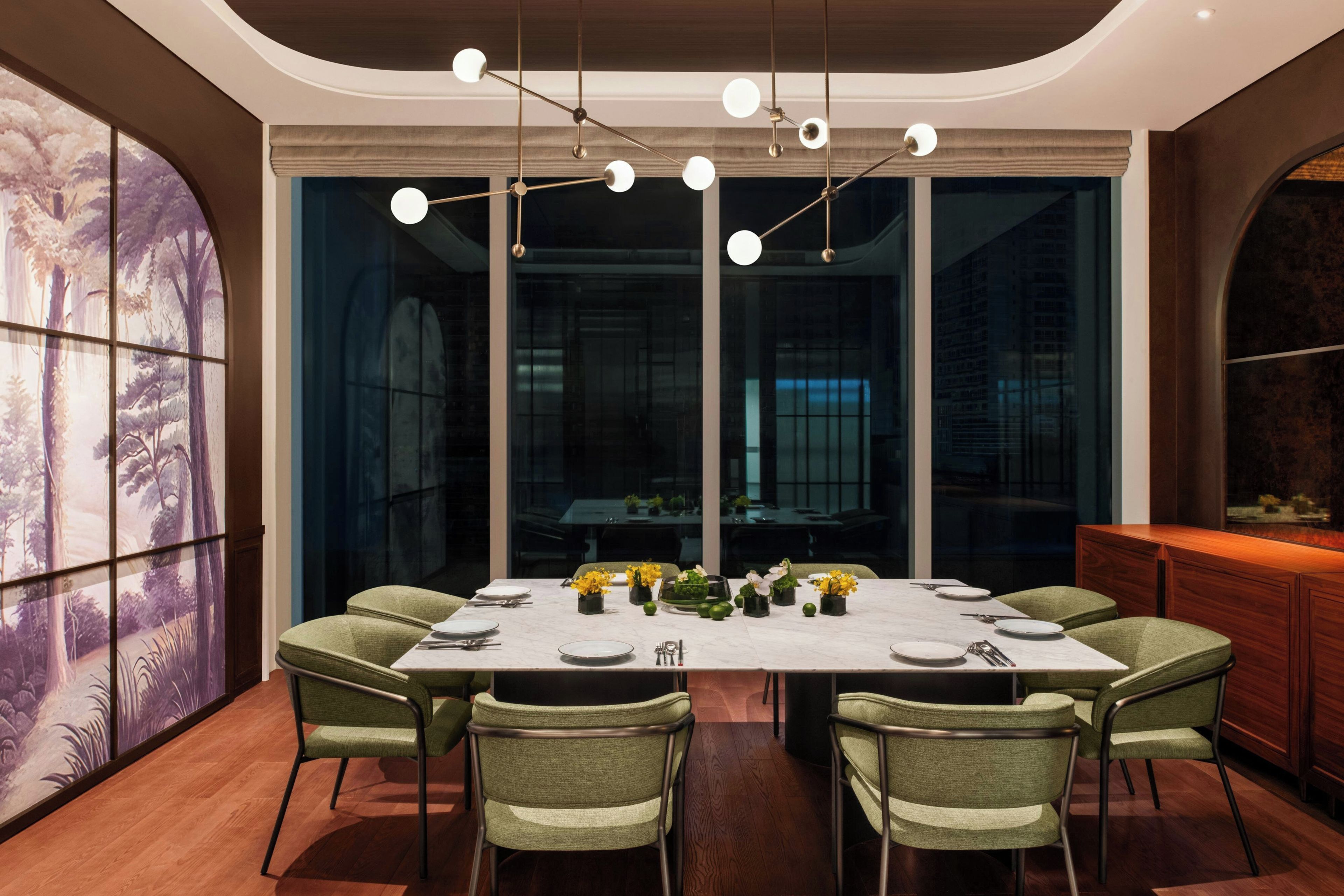 A modern dining room with a large table set for six, surrounded by green upholstered chairs.