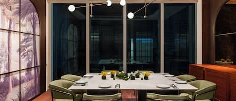 A modern dining room with a large table set for six, surrounded by green upholstered chairs.