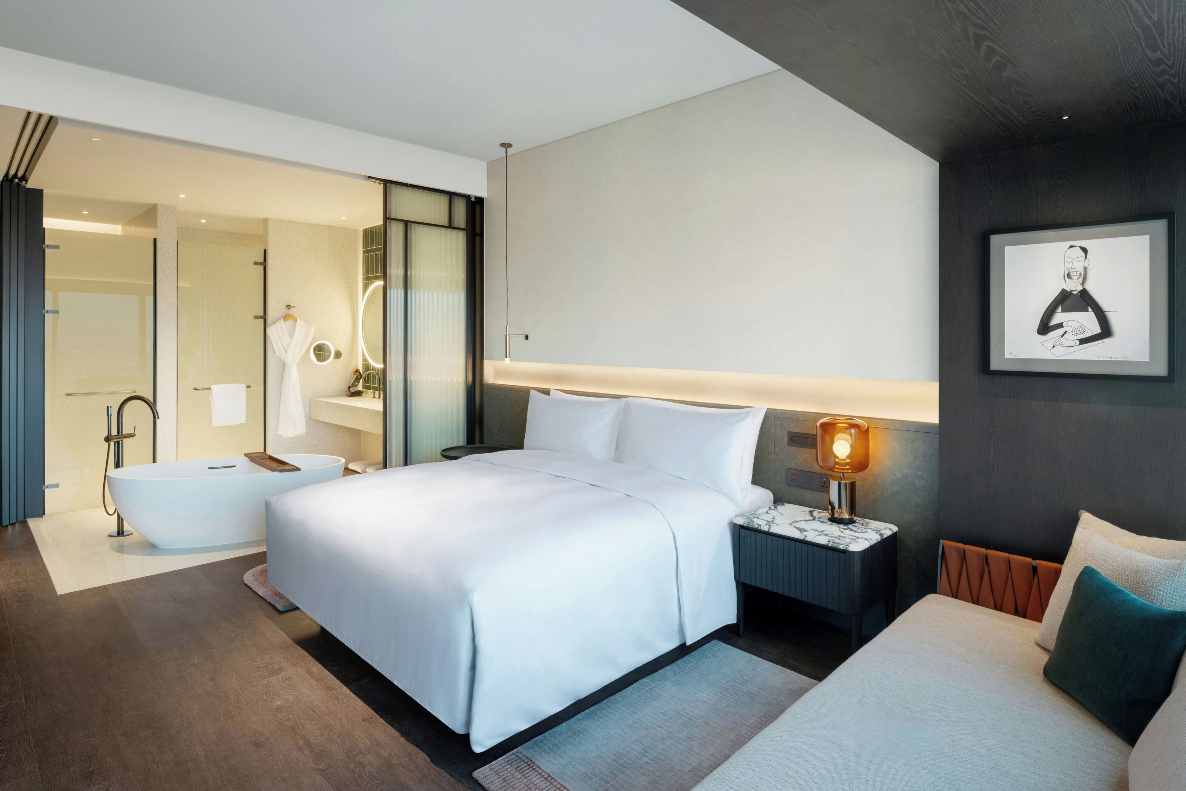 A modern hotel room with a large bed, a separate sitting area, a bathtub, and a bathroom with a glass shower enclosure.