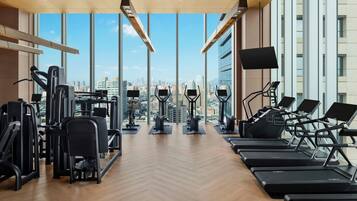 A gym with exercise equipment, large windows, and a city view.