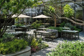 An outdoor dining area with tables and chairs, surrounded by greenery and trees.