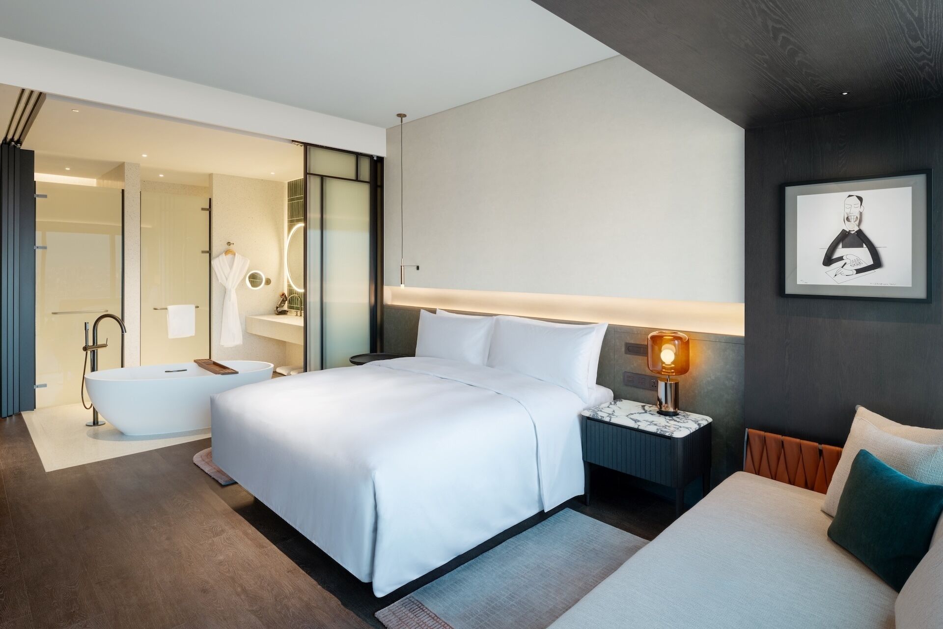 A modern hotel room with a large bed, a bedside table with a lamp, a bathroom with a bathtub, and a large mirror.