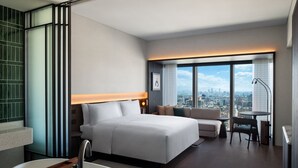 Een moderne hotelkamer met een groot bed, een zithoek, een bureau en uitzicht over de stad.